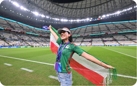 Female Mexico supporter posing with a Mexican flag inside a stadium during a match.
