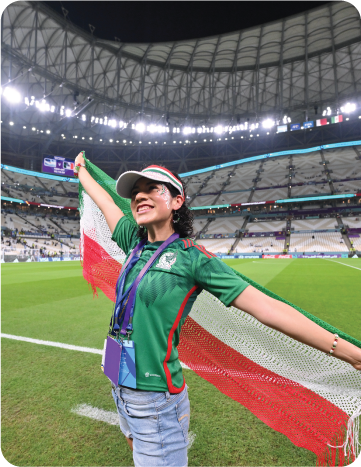 Female Mexico supporter posing with a Mexican flag inside a stadium during a match.